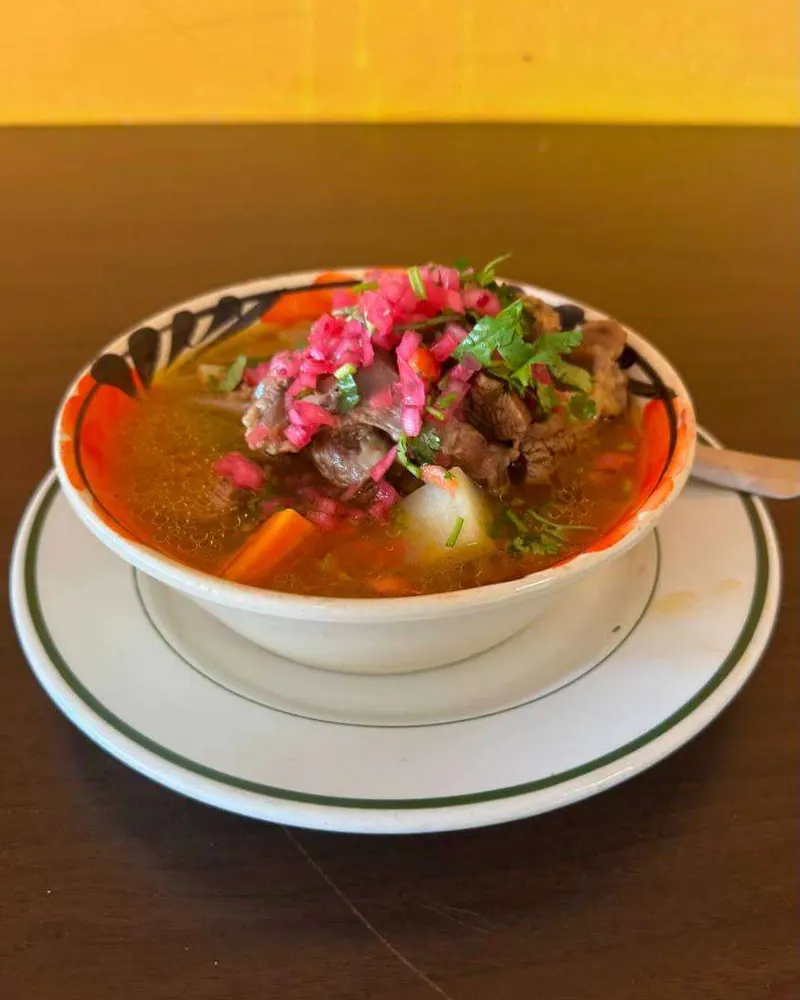 A bowl of caldo de res with beef, potato and carrot, topped with pickled onion and cilantro